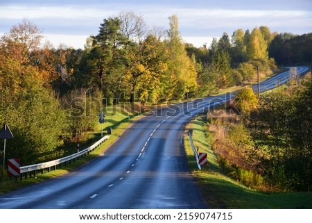An empty asphalt highway surrounded with colorful trees captured at daytime in autumn