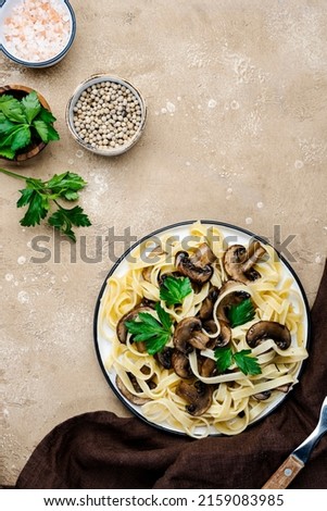 Cooked pasta with mushrooms with parsley on plate on beige stone kitchen table background, top view. Vegan cooking and eating, italian cuisine recipe Royalty-Free Stock Photo #2159083985