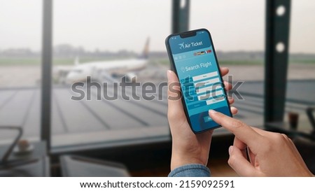 User holding a smartphone and booking cheap flights online, airport in the background, POV shot Royalty-Free Stock Photo #2159092591