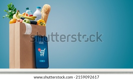 Grocery shopping app and grocery bag full of goods: online grocery shopping and home delivery concept, copy space Royalty-Free Stock Photo #2159092617