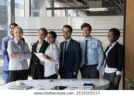 Multiethnic employees standing in modern office boardroom looking at camera making team picture, smile pose for photo at workplace, show unity and cooperation. Teamwork, leadership and career concept