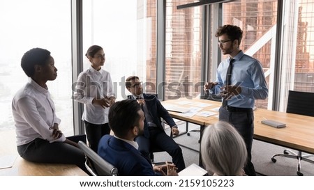 Team leader makes speech to diverse teammates during briefing in modern skyscraper office boardroom. Supervisor meets with company employees. Coaching event, leadership, business task solution concept Royalty-Free Stock Photo #2159105223