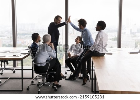 Colleagues gather in boardroom, planning work, share ideas, two friendly male workmates give high five start collaborative project, congratulate with result, express regard. Teamwork, support concept Royalty-Free Stock Photo #2159105231