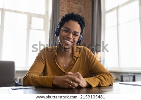Smiling African woman in headphones looks at camera take part in virtual meeting by study or business using video conference application. Modern tech, remote communication, video call event concept Royalty-Free Stock Photo #2159105481