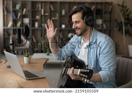 Smiling man musician vlogger influencer wave hand to laptop webcam greet channel audience before present new song with guitar. Young guy music teacher make video call to student ready to start class