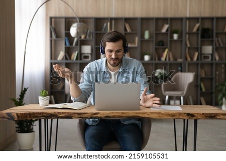 Teaching on distance. Confident male teacher in headset and glasses sit at desk give remote video class in conference app using laptop webcam. Young man tutor coach talk before pc hold online training Royalty-Free Stock Photo #2159105531