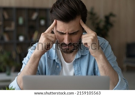 Mental tension. Stressed male sit by pc contemplate think hard with closed eyes touch forehead with fingers. Young man freelancer try to concentrate control emotions feel information overload headache