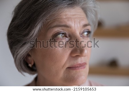 Serious thoughtful senior mature woman looking away in deep thought. Concerned grey haired retired lady face with brown eyes, wrinkles close up. Elderly age, mental health, dementia concept Royalty-Free Stock Photo #2159105653