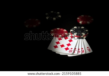 Playing cards on a black table with a royal flush poker winning combination and chips in the background.