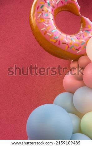colorful balloons in front of a pink wall with a decorative donut