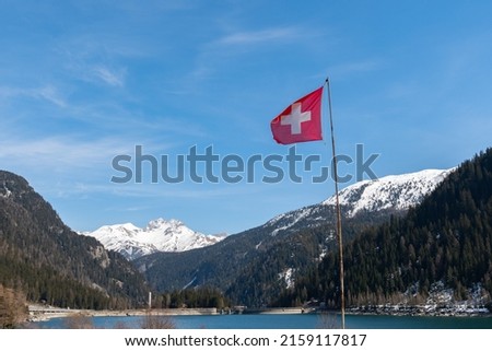 Sufers, Grison, Switzerland, April 12, 2022 Waving swiss flag in a snow covered alpine scenery on a beautiful lake