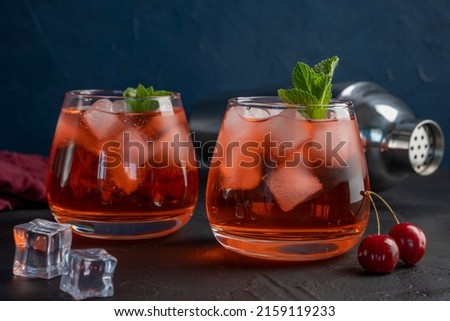 Cherry cocktail in glass on blue background. Summer iced beverage