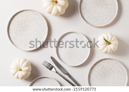 Some white ceramic plates with tableware and pumpkins serving background on white, mock up, top view Royalty-Free Stock Photo #2159120771