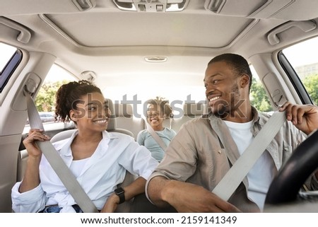 Joyful Black Family Riding New Car Enjoying Summer Road Trip Together. Parents And Little Daughter Sitting In Automobile, Putting On Seat Belts For Safety. Transportation, New Auto Concept Royalty-Free Stock Photo #2159141349
