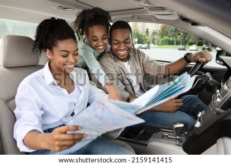 Happy African American Parents And Daughter Sitting In Car Holding Map For Navigation, Planning Summer Road Trip. Family Enjoying Auto Tourism Traveling Together On Vacation Royalty-Free Stock Photo #2159141415