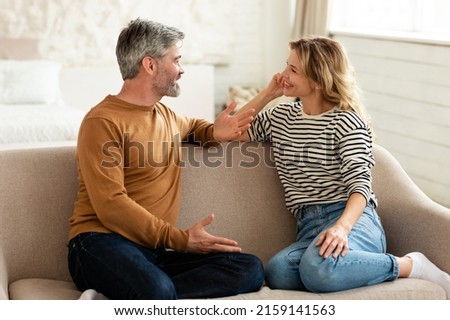 Cheerful Middle Aged Couple Talking And Flirting Enjoying Conversation Spending Time Together Sitting On Sofa At Home. Happy Marriage And Romantic Relationship Concept Royalty-Free Stock Photo #2159141563