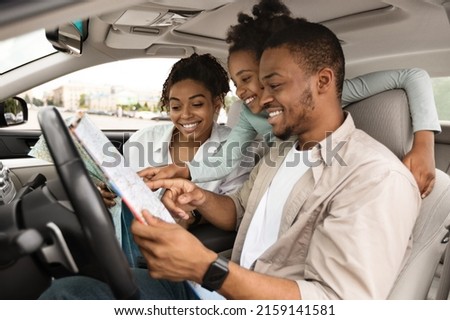 Road Trip Adventure. Happy African American Family Holding Map Sitting In Car Choosing Destination For Vacation. Travel By Automobile. Transportation And Navigation. Selective Focus, Side View Royalty-Free Stock Photo #2159141581