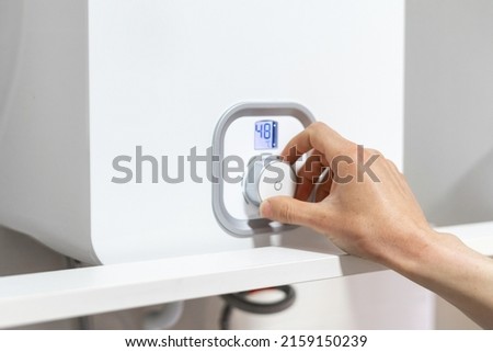 Woman hand turning regulate knob, adjusting temperature on gas or water boiler, cropped view. Female choose eco mode on heating system at kitchen or bathroom. Concept of household equipment Royalty-Free Stock Photo #2159150239