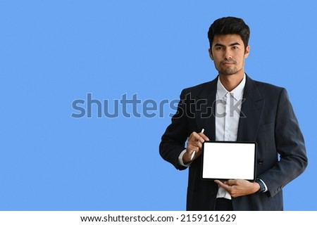 Asian Indian male in suit holding a digital tablet with blank white screen over a light blue isolated background. Business and financial concepts.