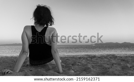 Unhappy single woman sitting on sand, looking at distant sea or seascape horizon. Missing someone concept idea. Time to go, say goodbye or good bye. Empty copy space for advertising banners.
