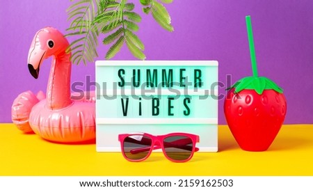 Inflatable flamingo for drink, pink sunglasses, strawberry mug and lightbox with quote Summer Vibes on bright background. Retro vibe or 80s, nostalgic style, retro aesthetic still life. Summer vacatio