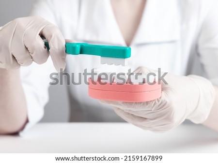 Dentist brushing teeth in jaw model. Stomatology, oral hygiene concept. Doctor in lab coat and gloves sitting at table and holding toothbrush and mouth layout. High quality photo