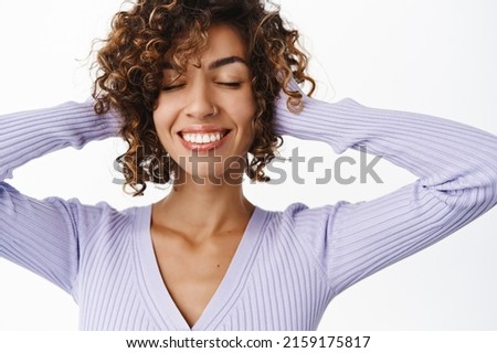 Haircare and women beauty. Attractive happy woman face, girl playing with curly hair, smiling and looking relaxed and carefree, standing over white background