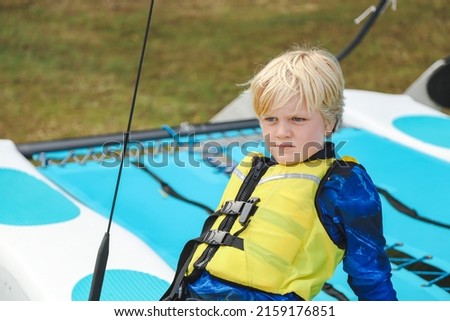 Young boy wearing yellow life jacket sitting on boat ready to go sailing Royalty-Free Stock Photo #2159176851