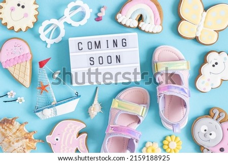 Coming soon. Motivational quote on lightbox and cute summer symbols on blue background. Top view, Flat lay. Creative inspirational summer concept.