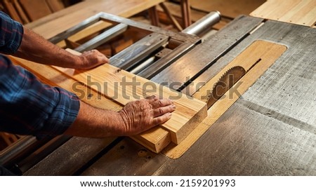 Closeup of wood cutting table with electric circular saw.  Senior Professional carpenter in uniform cutting wooden board at sawmill carpentry manufacturing . Sawing machine Royalty-Free Stock Photo #2159201993