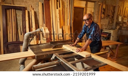 Wood cutting table with electric circular saw.  Senior Professional carpenter in uniform cutting wooden board at sawmill carpentry manufacturing . Sawing machine Royalty-Free Stock Photo #2159201999