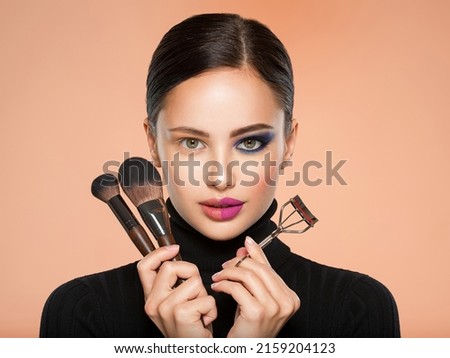 Portrait of a girl with  tools for making makeup near face.  One half face of a beautiful white woman with  bright makeup and the other is natural. Woman holds makeup brush and eyelash curler. Natural Royalty-Free Stock Photo #2159204123