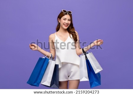 Smiling pretty Asian woman carrying shopping bags in purple color studio background