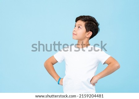 Handsome mixed race boy thinking and looking up with arms akimbo in isolated studio light blue color background Royalty-Free Stock Photo #2159204481