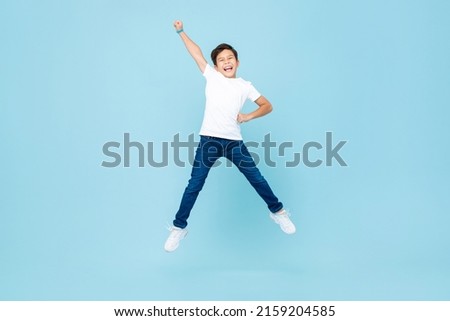 Cheerful Asian mixed race boy jumping and raising hand up in isolated light blue color studio background Royalty-Free Stock Photo #2159204585