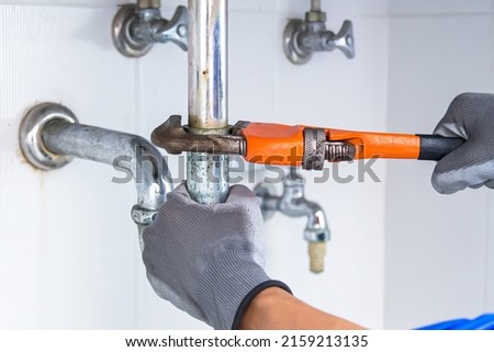 Technician plumber using a wrench to repair a water pipe under the sink. Concept of maintenance, fix water plumbing leaks, replace the kitchen sink drain, cleaning clogged pipes is dirty or rusty. Royalty-Free Stock Photo #2159213135