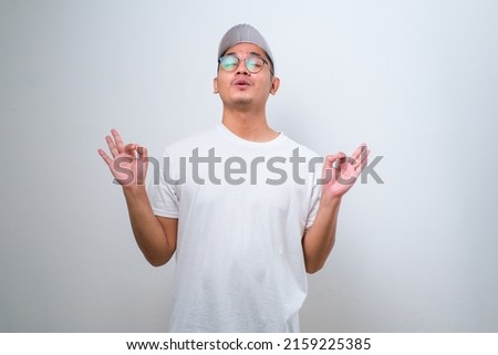 Young handsome asian delivery man wearing cap standing over isolated white background relax and smiling with eyes closed doing meditation gesture with fingers. Yoga concept.