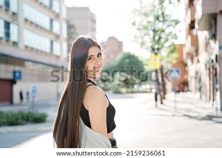 Portrait of beautiful smiling casual student girl dreamily looking in camera on street. Young caucasian woman with long hair