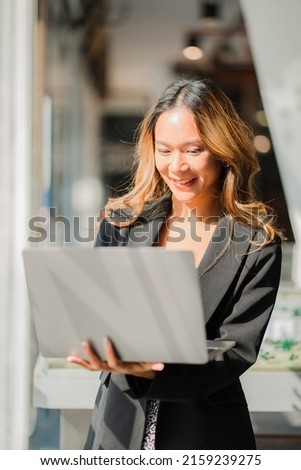 Asian businesswoman standing with laptop congratulating her achievements at company office