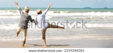 Asian senior couple wearing hat sunglasses  holding hands dancing  walking on the beach,Enjoy life on the beach after  elderly retired , Retirement  planning life insurance healthy lifestyle travel 