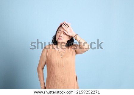 The senior Asian woman with brown dressed standing on the blue background.