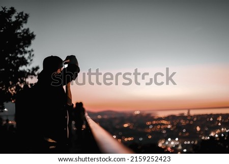 A caucasian photographer taking photos of the sunset with a bokeh lights background