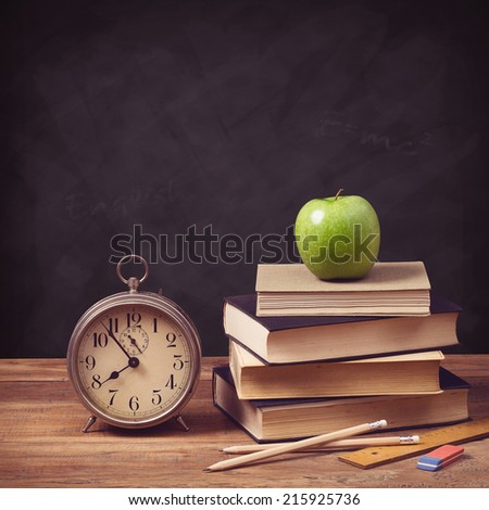 back to school concept with old schoolbooks, alarm clock and apple against a chalkboard background