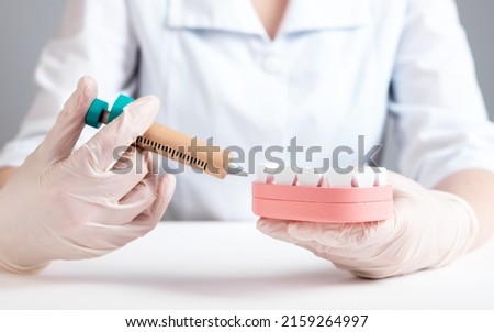 Dentist holding syringe for dental anesthesia and jaw model with teeth. Doctor in gloves injecting medicine to numb mouth area for tooth treatment or extraction. Stomatology concept. photo