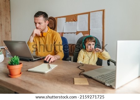 Little 5 years old girl with her father using laptops sitting at table. Family using technology at home. Parenthood during covid-19 lockdown. Daddy with her daughter working at home. Selective focus. Royalty-Free Stock Photo #2159271725