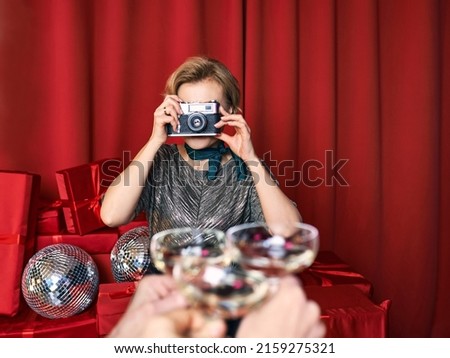 Cheerful beautiful photographer woman at the party celebration on red curtains background. Profession, party concept
