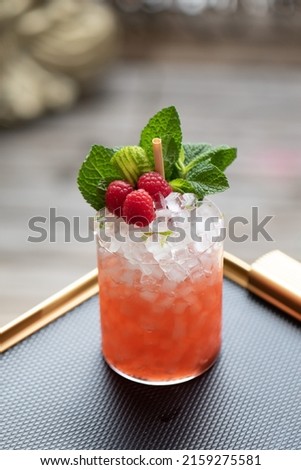 Tropical Cocktail with pebble ice plus mint and raspberry garnish in tumbler glass on tray