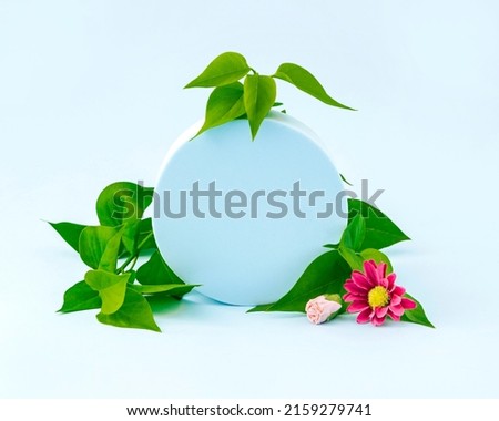 Summer and spring idea with a circular frame, leaves with pink flowers, on a sky blue background with copy space. Retro aesthetic concept of the 80s or 90s. Cosmetics and fashion minimal concept.