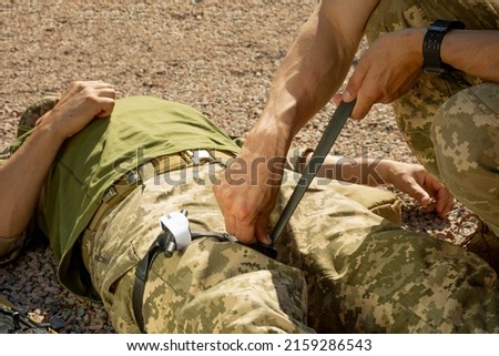 Army medics practice applying a tourniquet to the leg of a wounded soldier. Combat tactical equipment. Combat use Turnstile. The concept of military medicine. Royalty-Free Stock Photo #2159286543