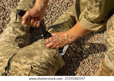 Army medics practice applying a tourniquet to the leg of a wounded soldier. Combat tactical equipment. Combat use Turnstile. The concept of military medicine. Royalty-Free Stock Photo #2159286547